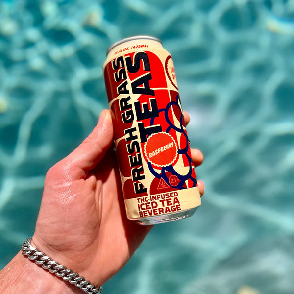 Hand holding a can of 'Fresh Grass Teas' by a pool