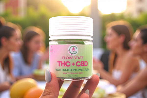 Hand holding a container labeled 'Flow State THC + CBD Watermelon Lime Tajin' with people in the background.