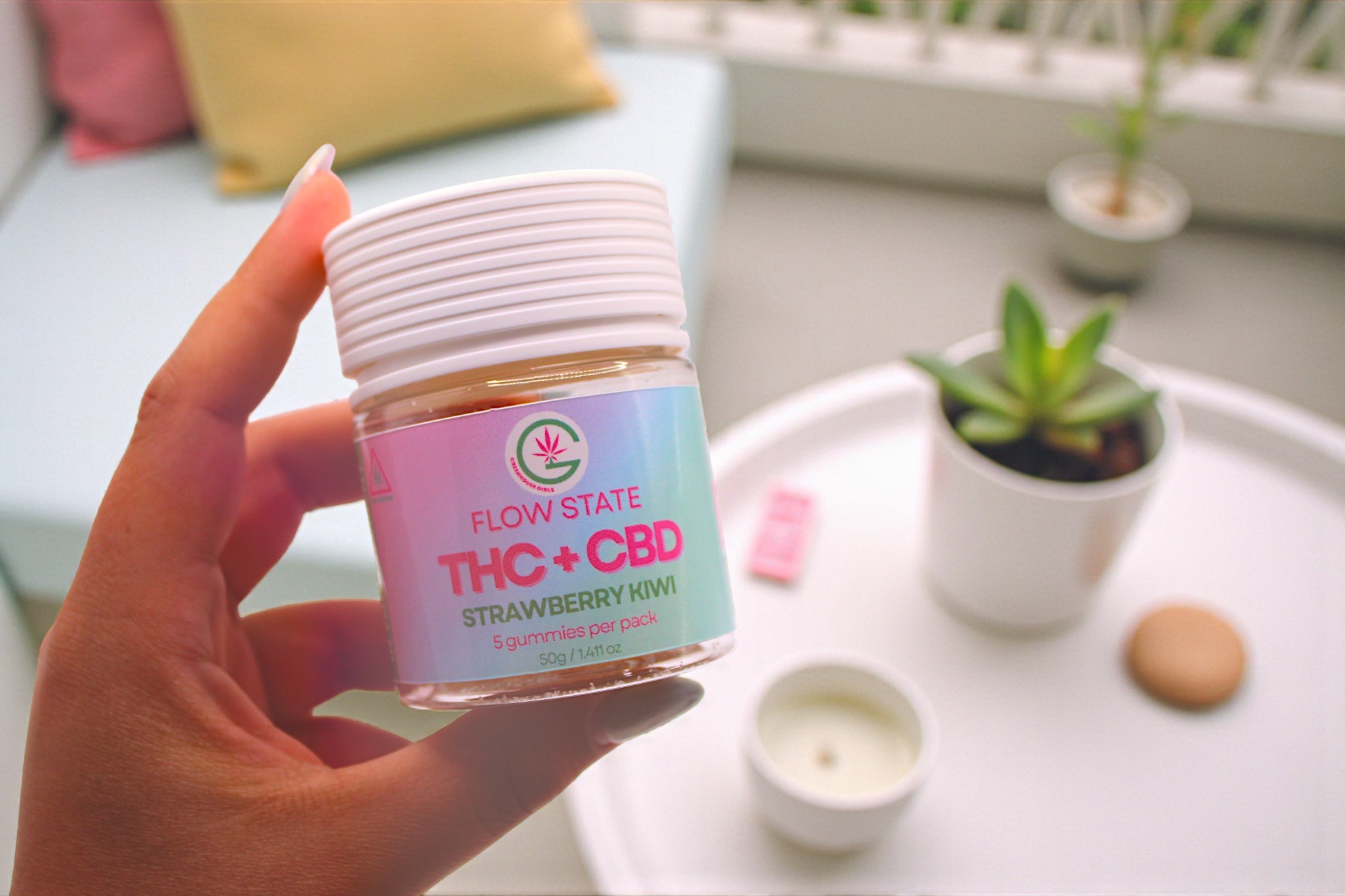 Hand holding a container labeled 'Flow State THC + CBD Strawberry Mint' on a blurred background