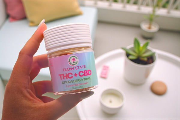 Hand holding a container labeled 'Flow State THC + CBD Strawberry Mint' on a blurred background