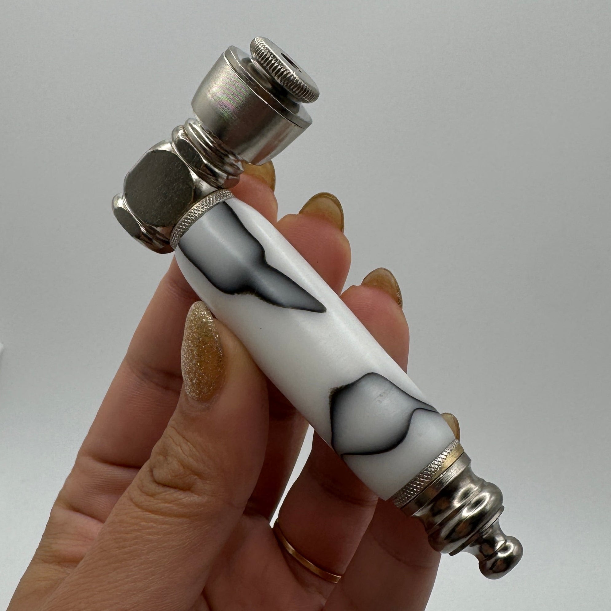Hand holding a white pepper grinder with black patterns against a white background