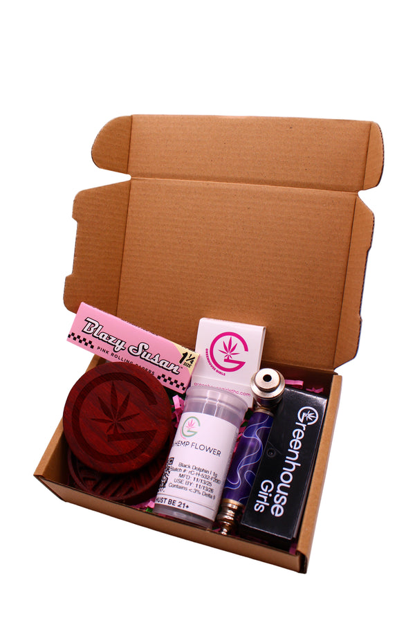 Open cardboard box with various items including a bottle labeled 'Greenhouse Girls' on a white background