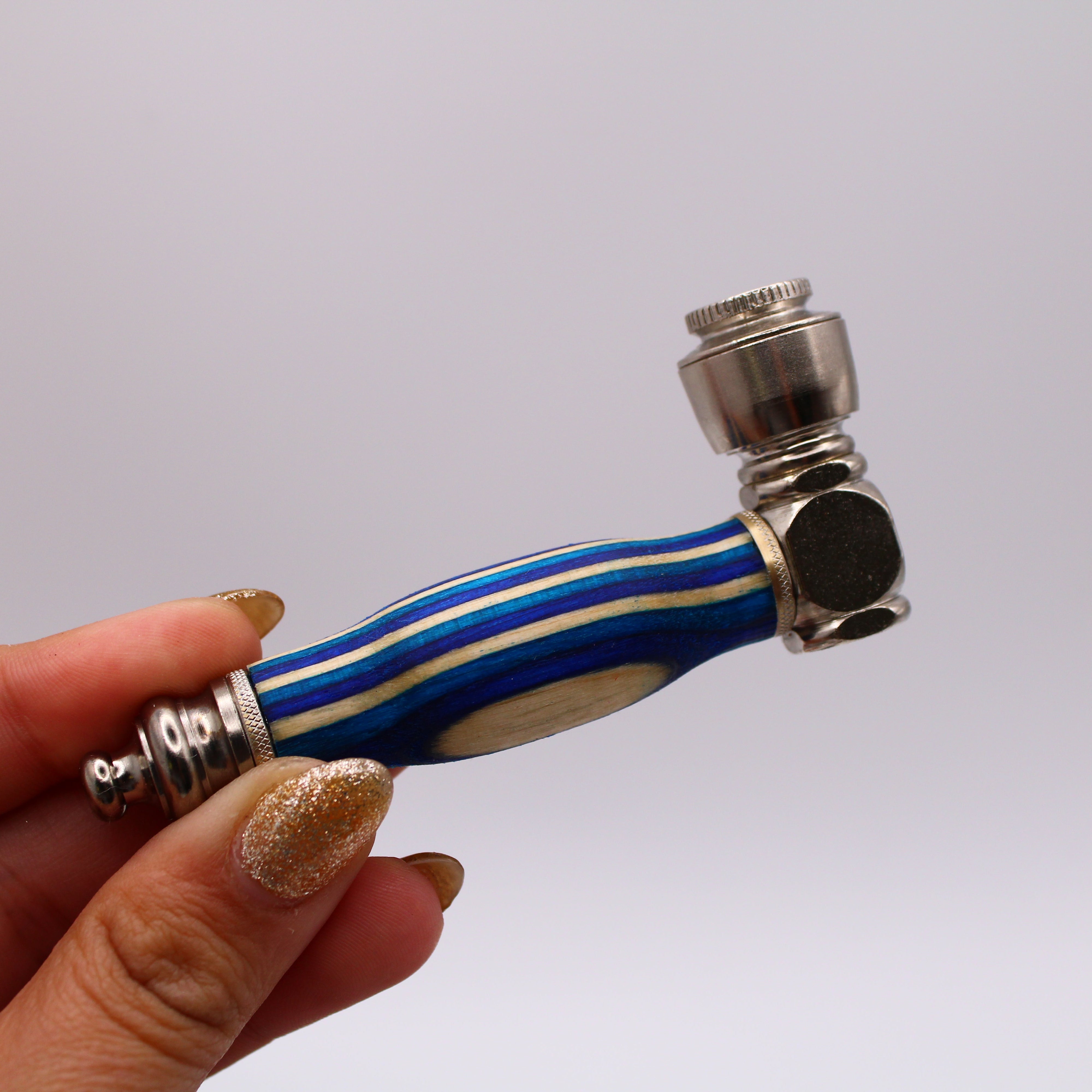 Hand holding a small pipe with blue and silver design against a plain background