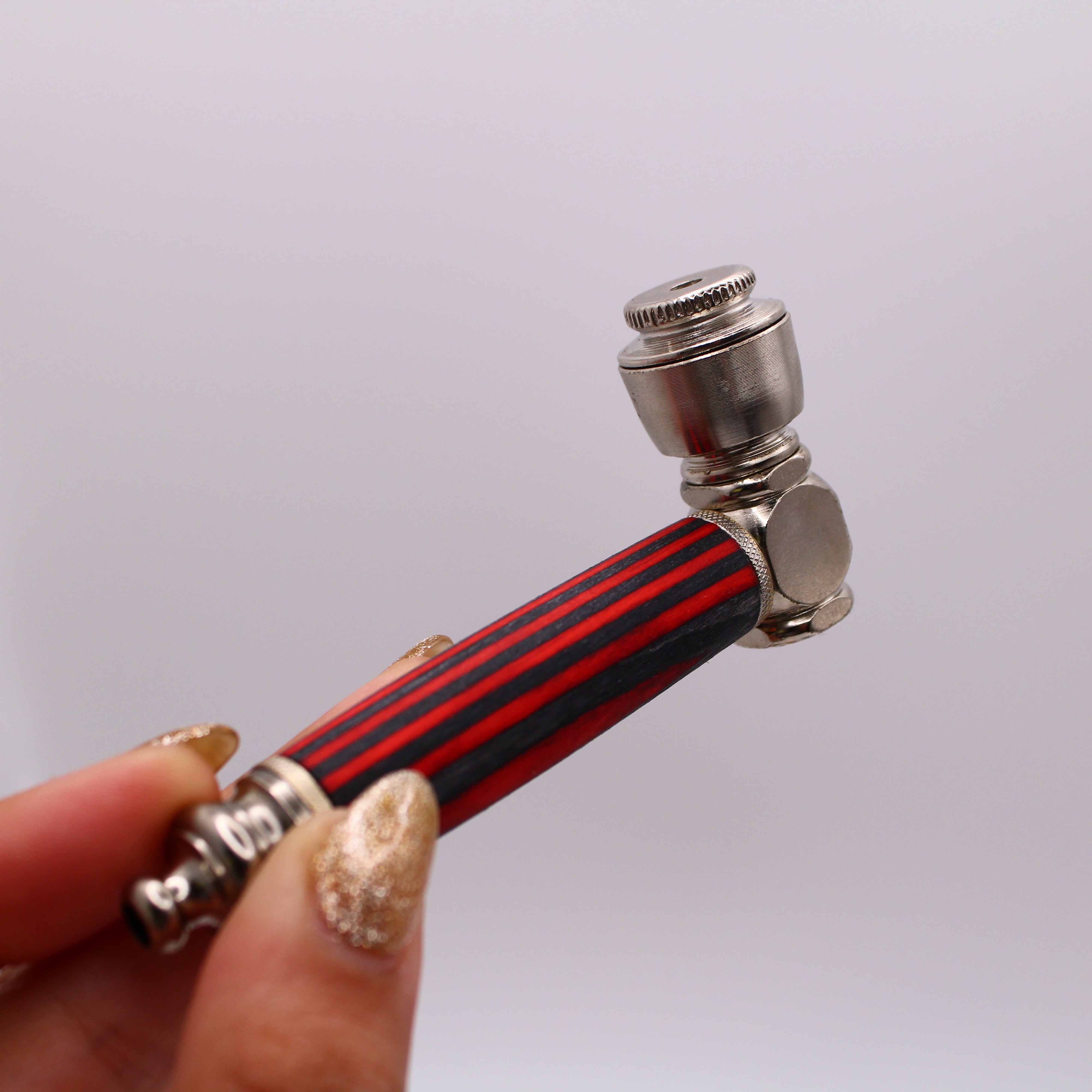 Hand holding a small pipe with red and black striped design on a white background