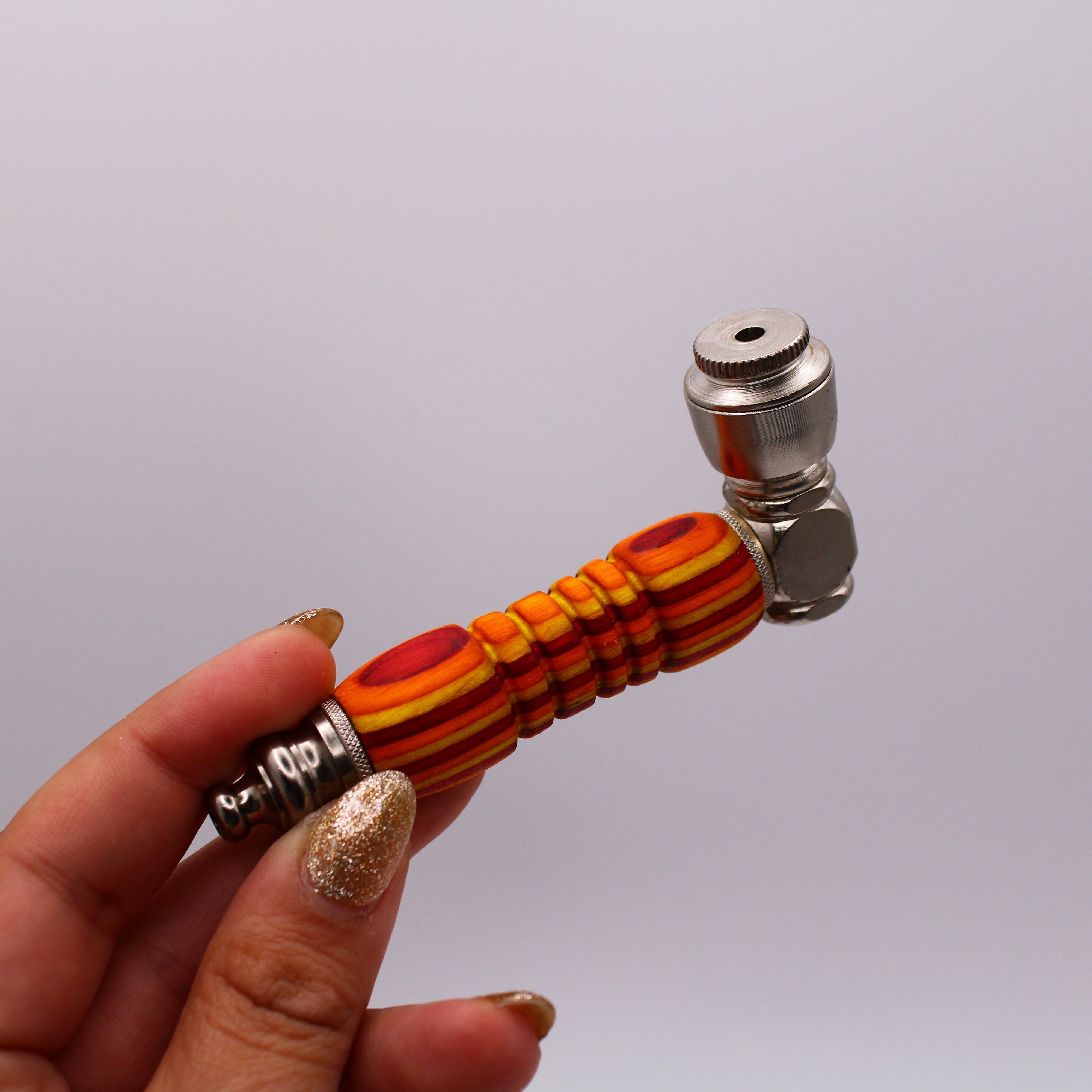 Hand holding a colorful smoking pipe with a silver fitting against a white background
