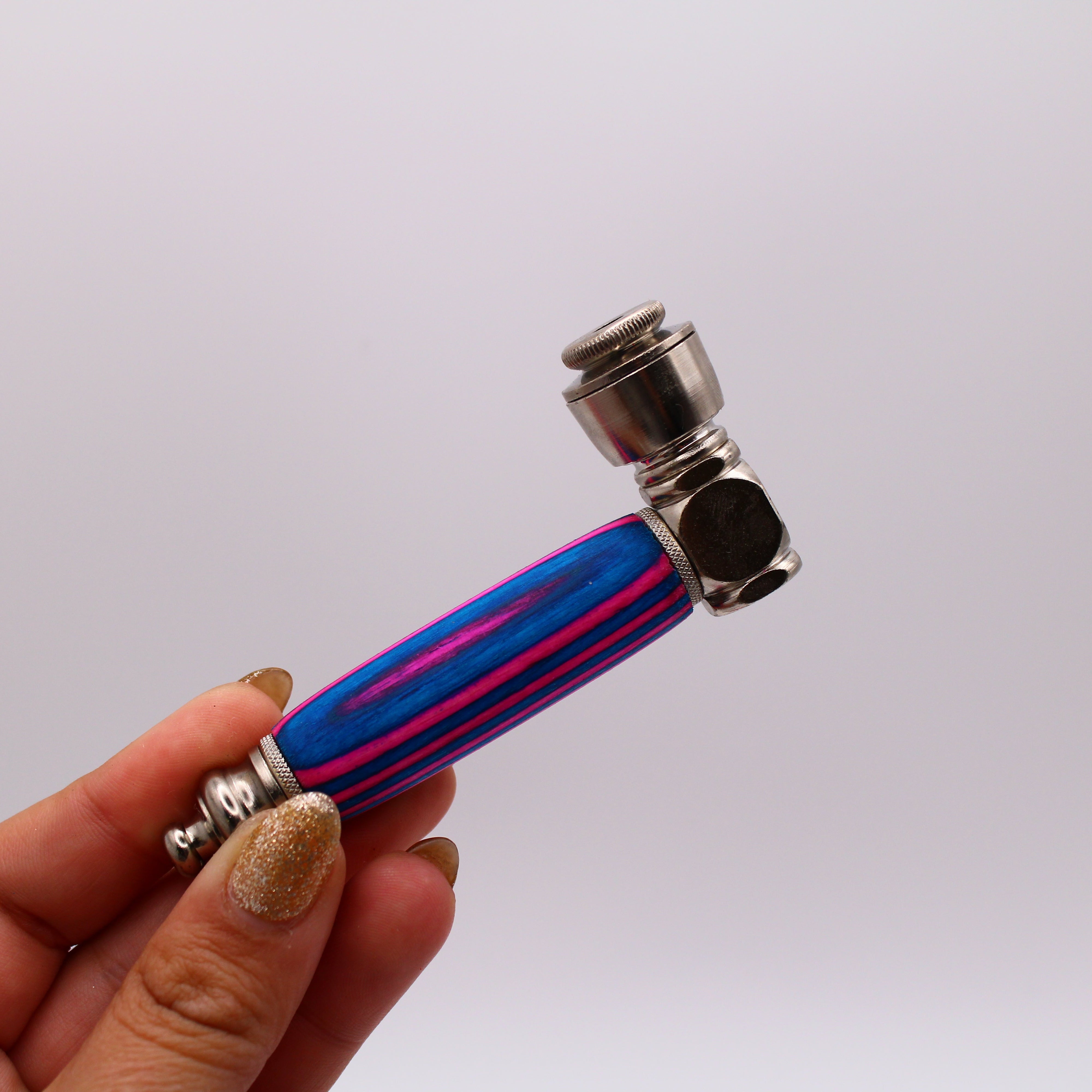 Hand holding a small pipe with blue and pink handle against a white background