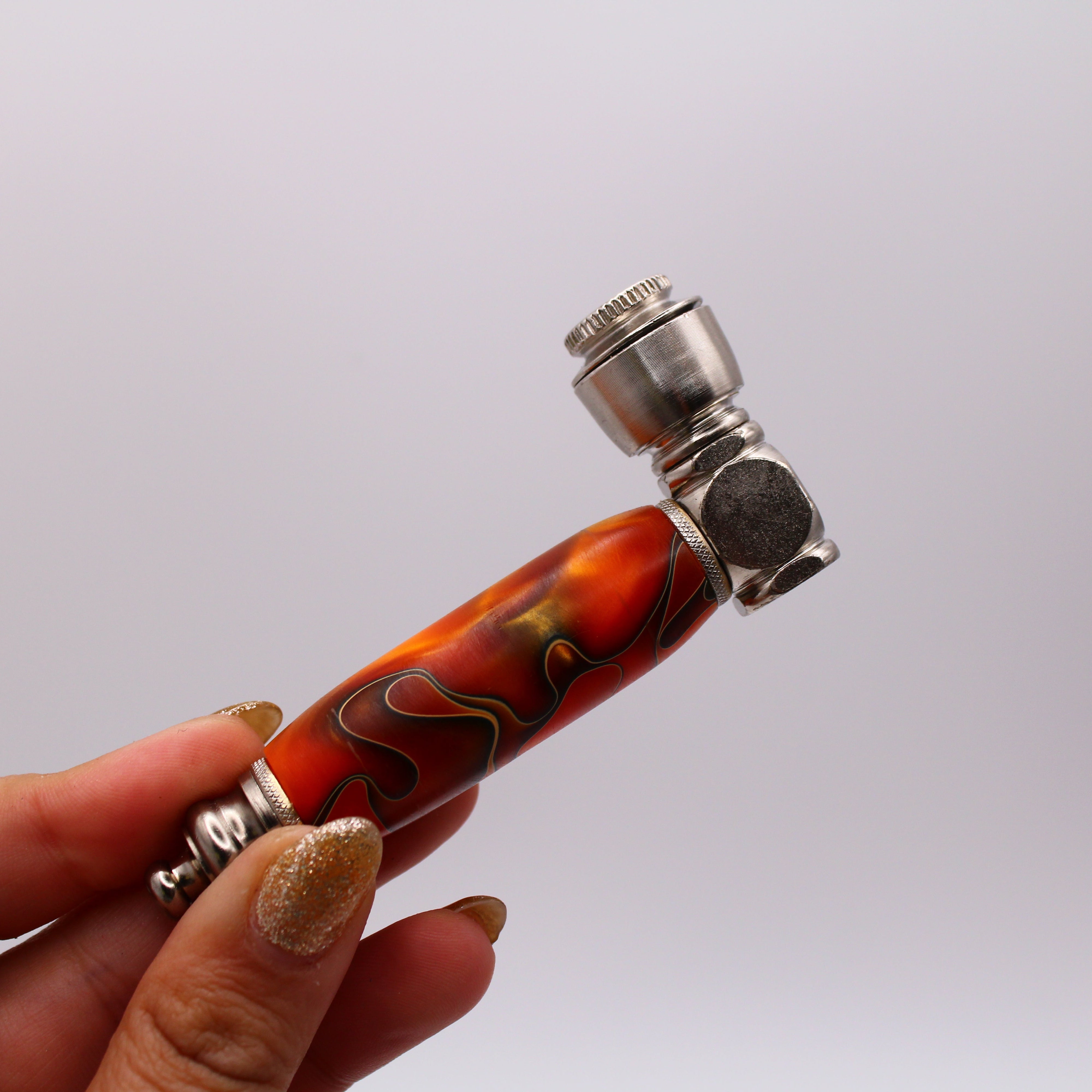 Hand holding a smoking pipe with a decorative orange and black design on a white background