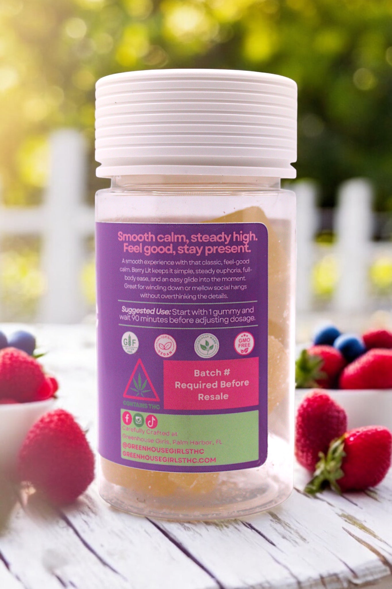 Jar with a purple label surrounded by strawberries and blueberries on a wooden surface.