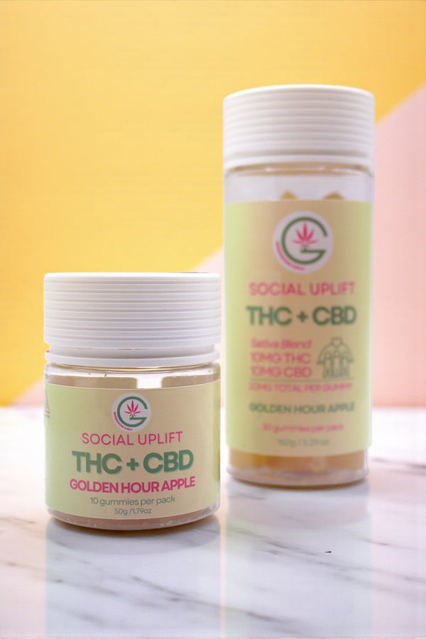 Two containers of Social Uplift THC + CBD gummies on a marble surface with a yellow background