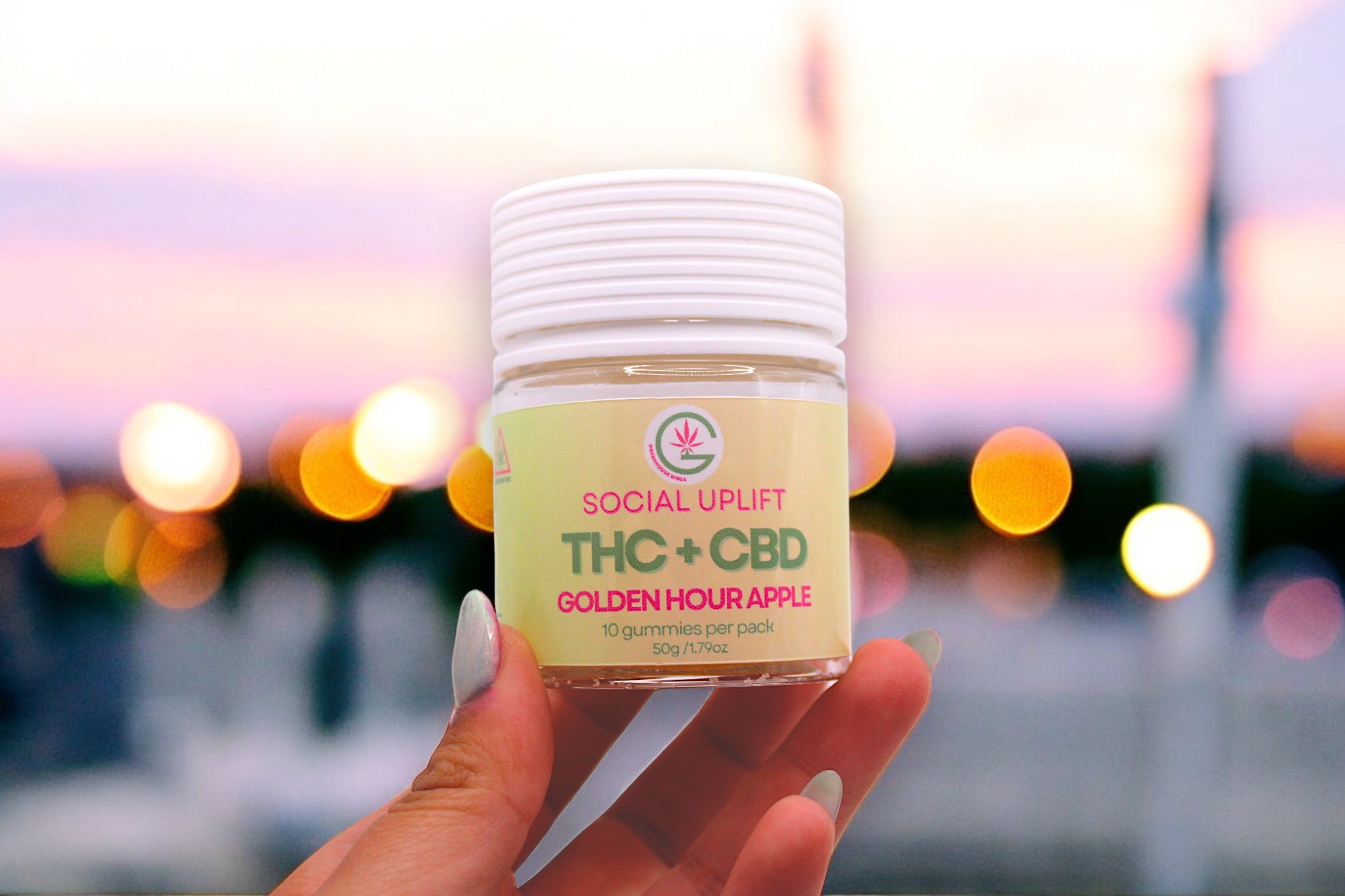 Hand holding a jar labeled 'SOCIAL UPLIFT THC + CBD GOLDEN HOUR APPLE' against a blurred background with lights.