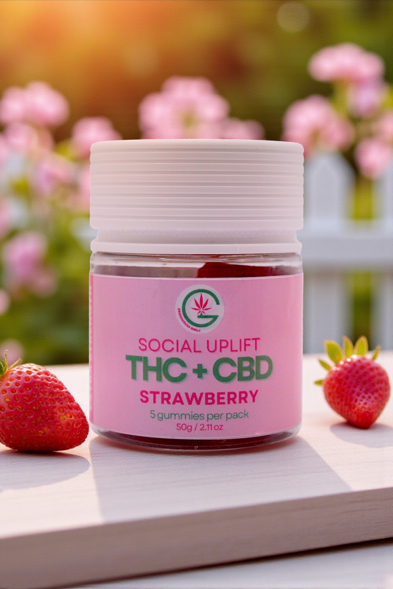 Jar of Social Uplift THC + CBD Strawberry gummies with strawberries on a wooden surface and blurred flowers in the background.