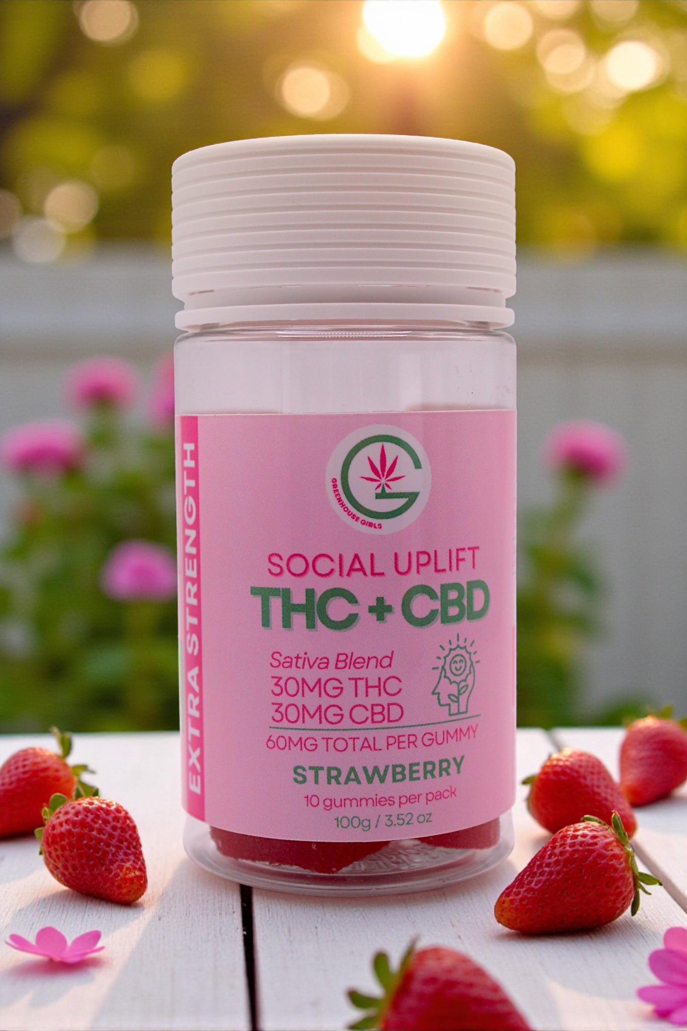 Bottle of Social Uplift THC + CBD gummies with strawberries on a table outdoors.
