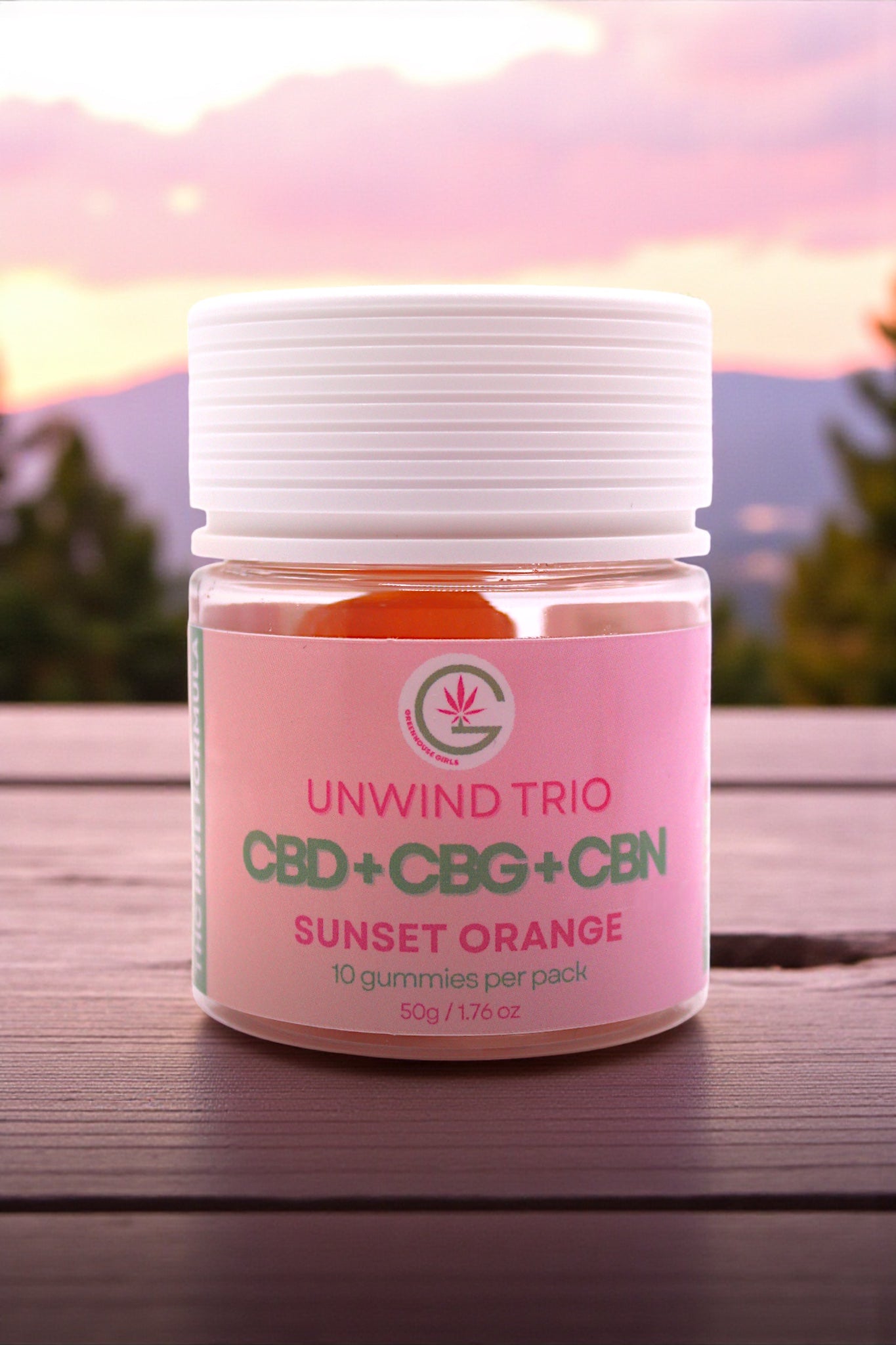 Jar of 'Unwind Trio' CBD+CBG+CBN gummies with a pink label on a wooden surface.