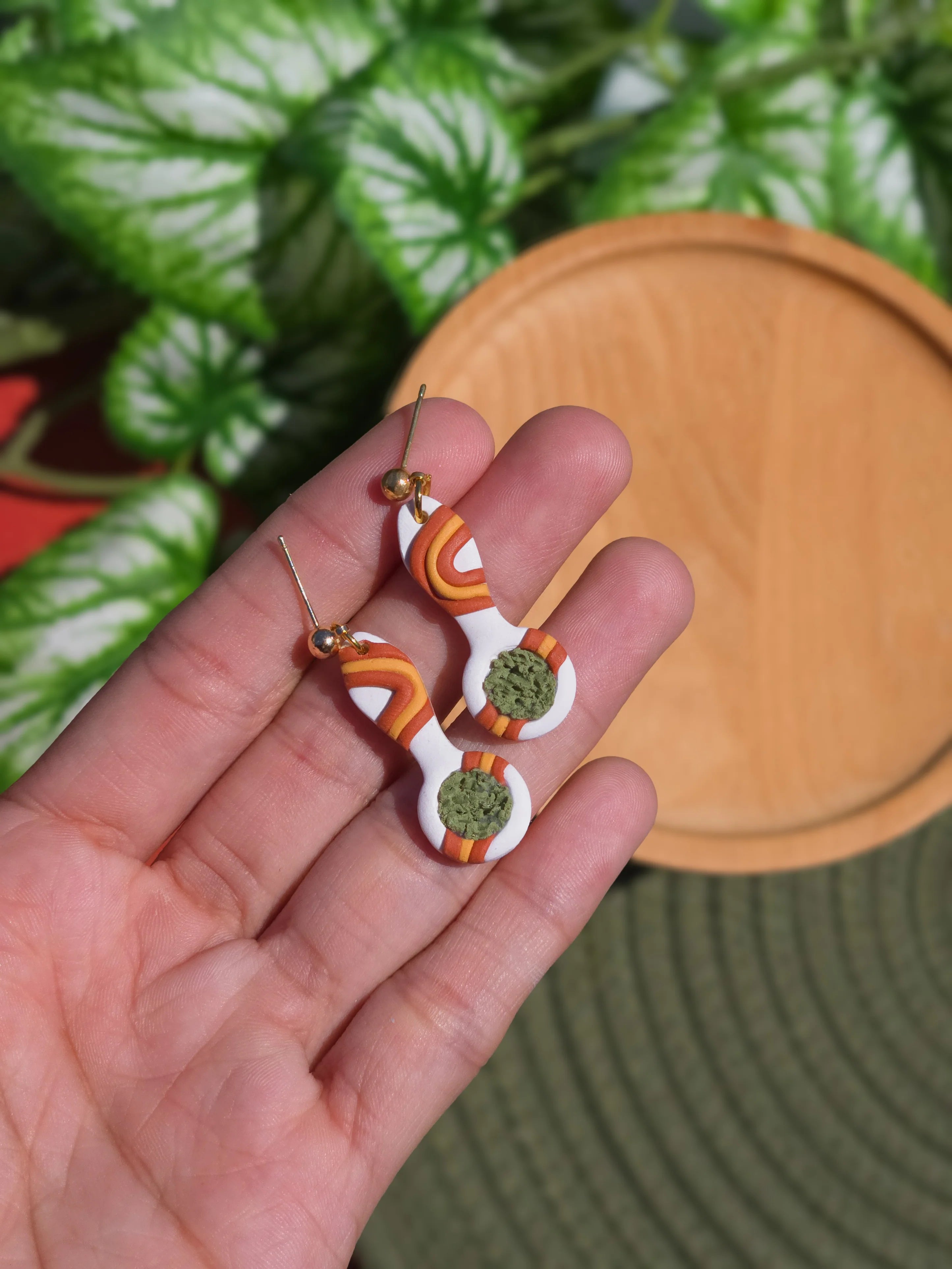 cannabis weed marijuana earrings handmade in hand over plants 
