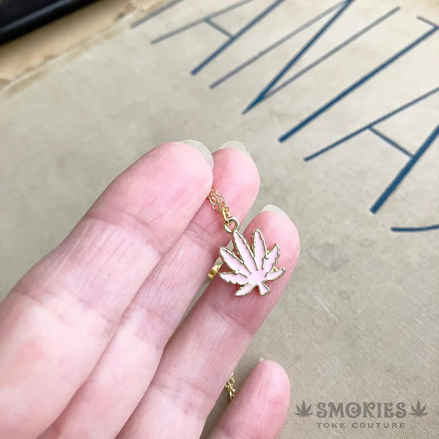 Gold necklace with a leaf pendant held by a hand on a textured surface.