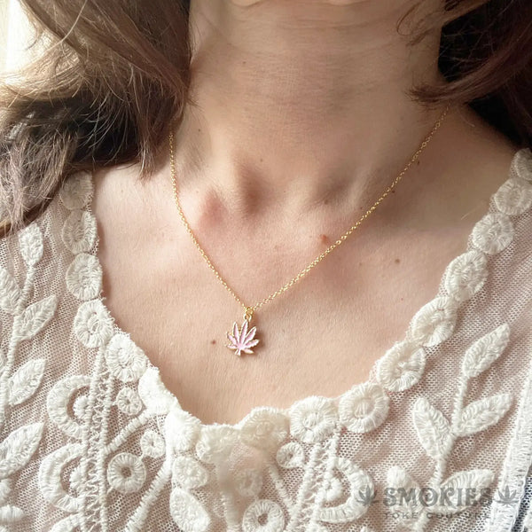 Close-up of a person wearing a gold necklace with a weed leaf pendant, against a white lace garment.
